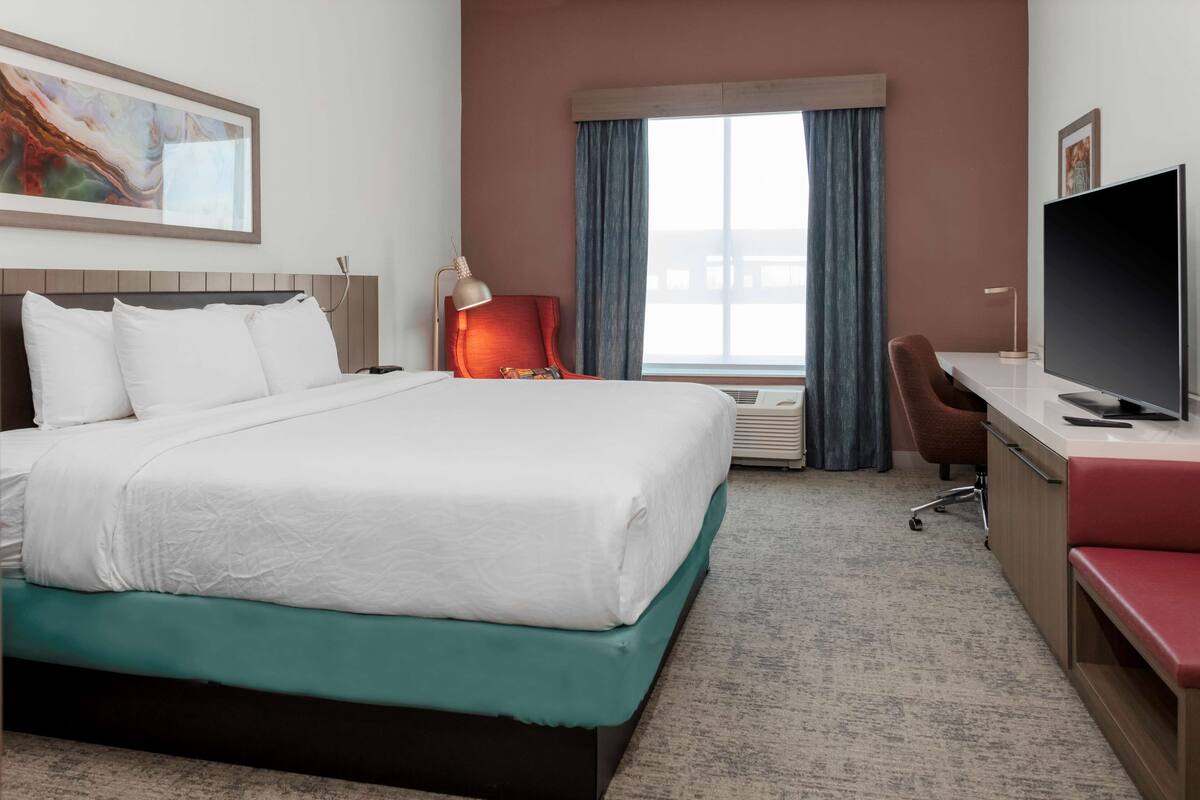 A hotel room with a bed, a desk, a TV, a chair, and a window with curtains.