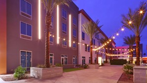 A modern hotel with a courtyard, palm trees, and string lights. - Hilton Garden Inn Chandler Downtown (Chandler)