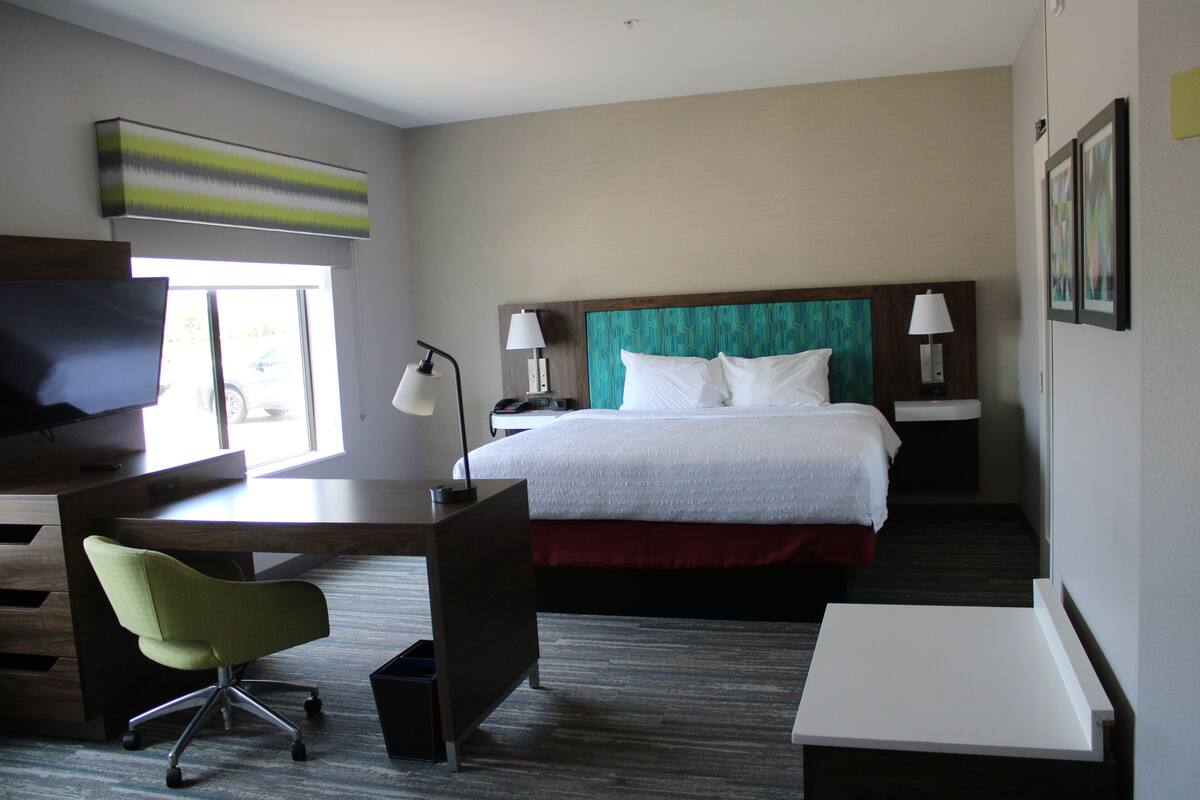 A hotel room with a bed, desk, chair, and a television.