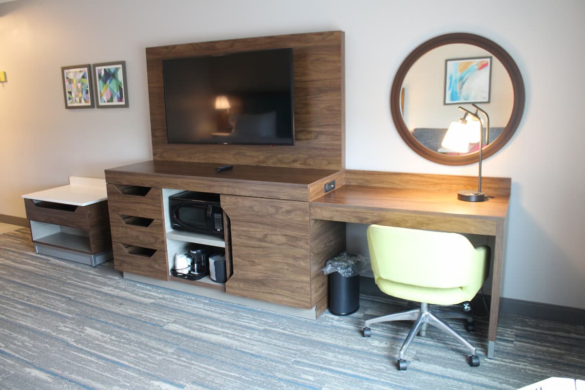 A modern hotel room with a wooden desk, a flat-screen TV, a yellow office chair, and a small trash bin.