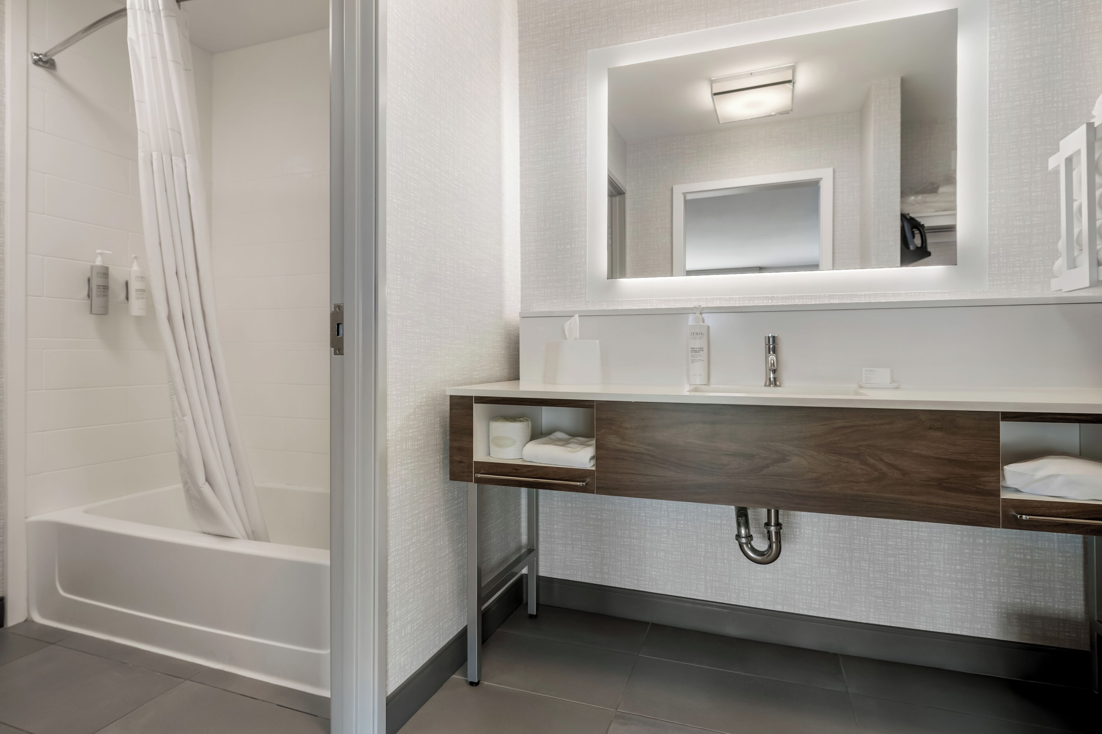 Un baño moderno con ducha a nivel, tocador con espejo y barra para toallas.