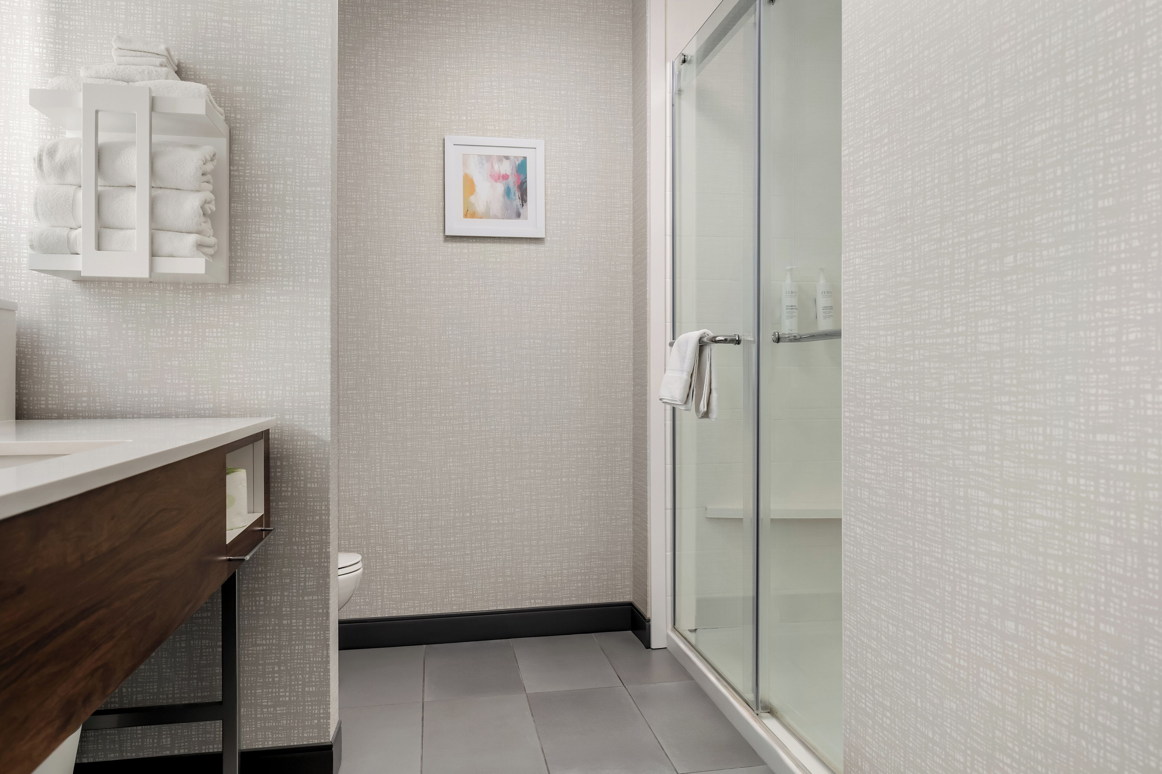 A modern bathroom with a glass shower enclosure, a white sink with a wooden countertop, and a towel rack.