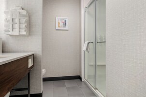 Un baño moderno con cabina de ducha de vidrio, lavamanos blanco sobre encimera de madera y un perchero para toallas.