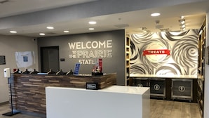 A hotel reception area with a 'Welcome to the Prairie State' sign, a counter, and a wall with a 'Treats' sign.