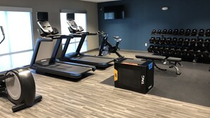 A gym with treadmills, a stationary bike, and a bench press. There are dumbbells on shelves and a large mirror on the wall.