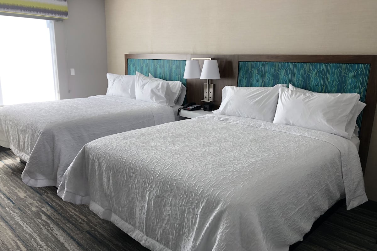 Two double beds with white linens, a nightstand with a lamp, and a patterned headboard.