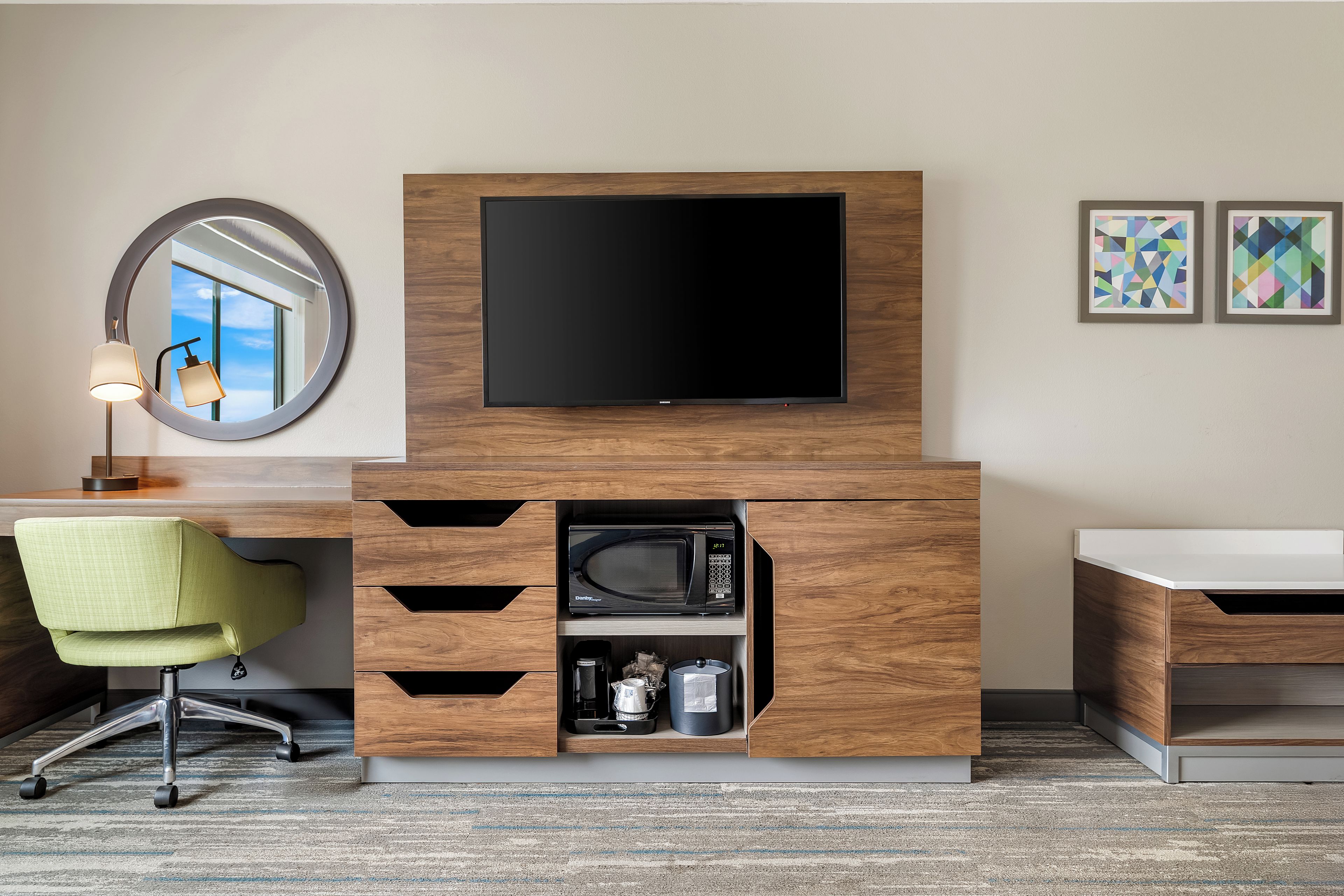 Een hotelkamer met een flatscreen televisie bevestigd aan een houten kast, een groene stoel, een koffieapparaat en een magnetron.