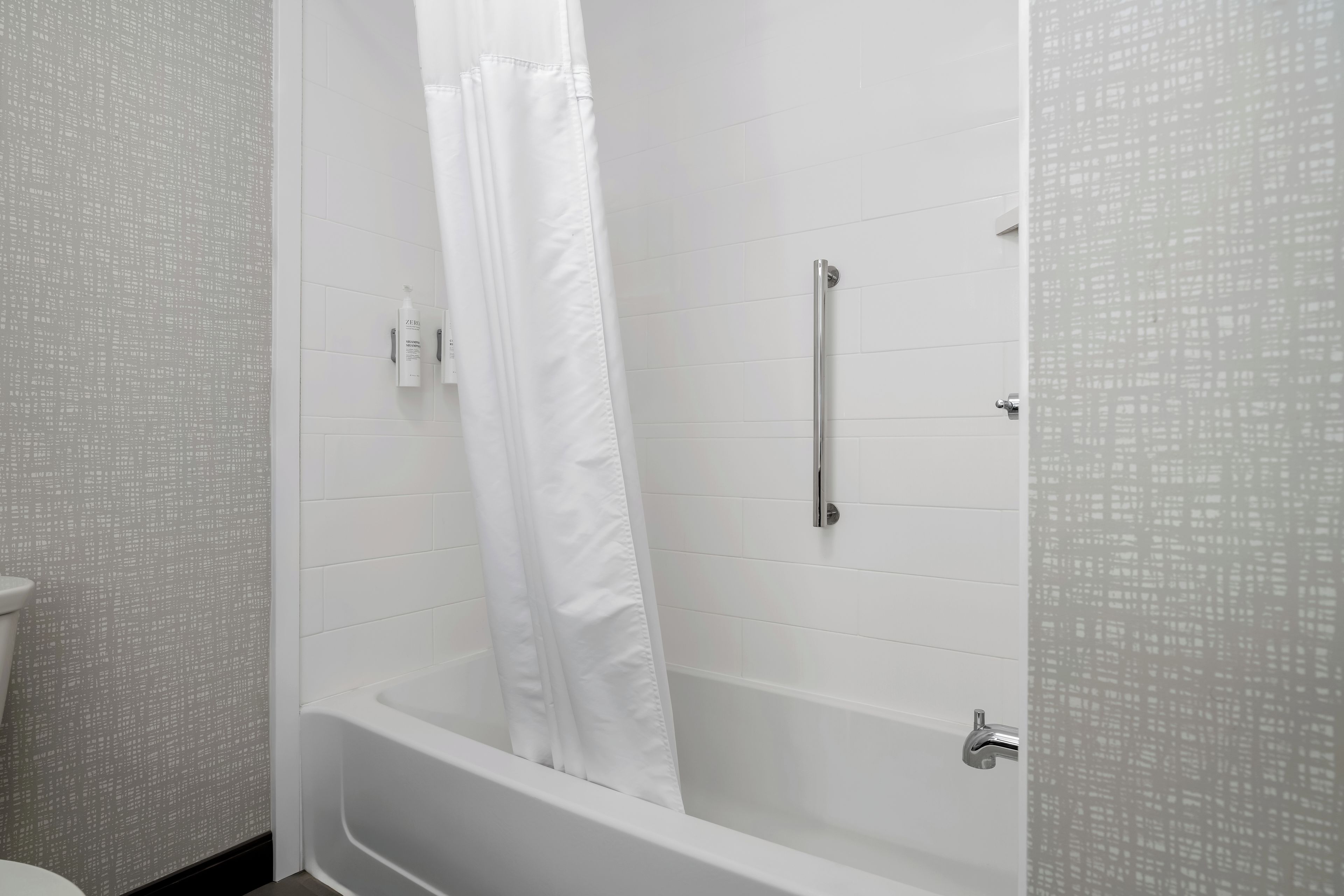 Un bagno con una vasca, una tenda doccia e una maniglia di sostegno.