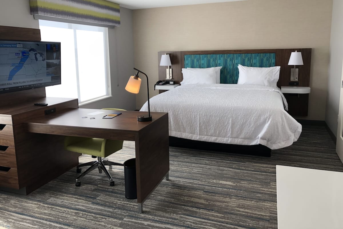 A hotel room with a bed, desk, and a television displaying a weather forecast.