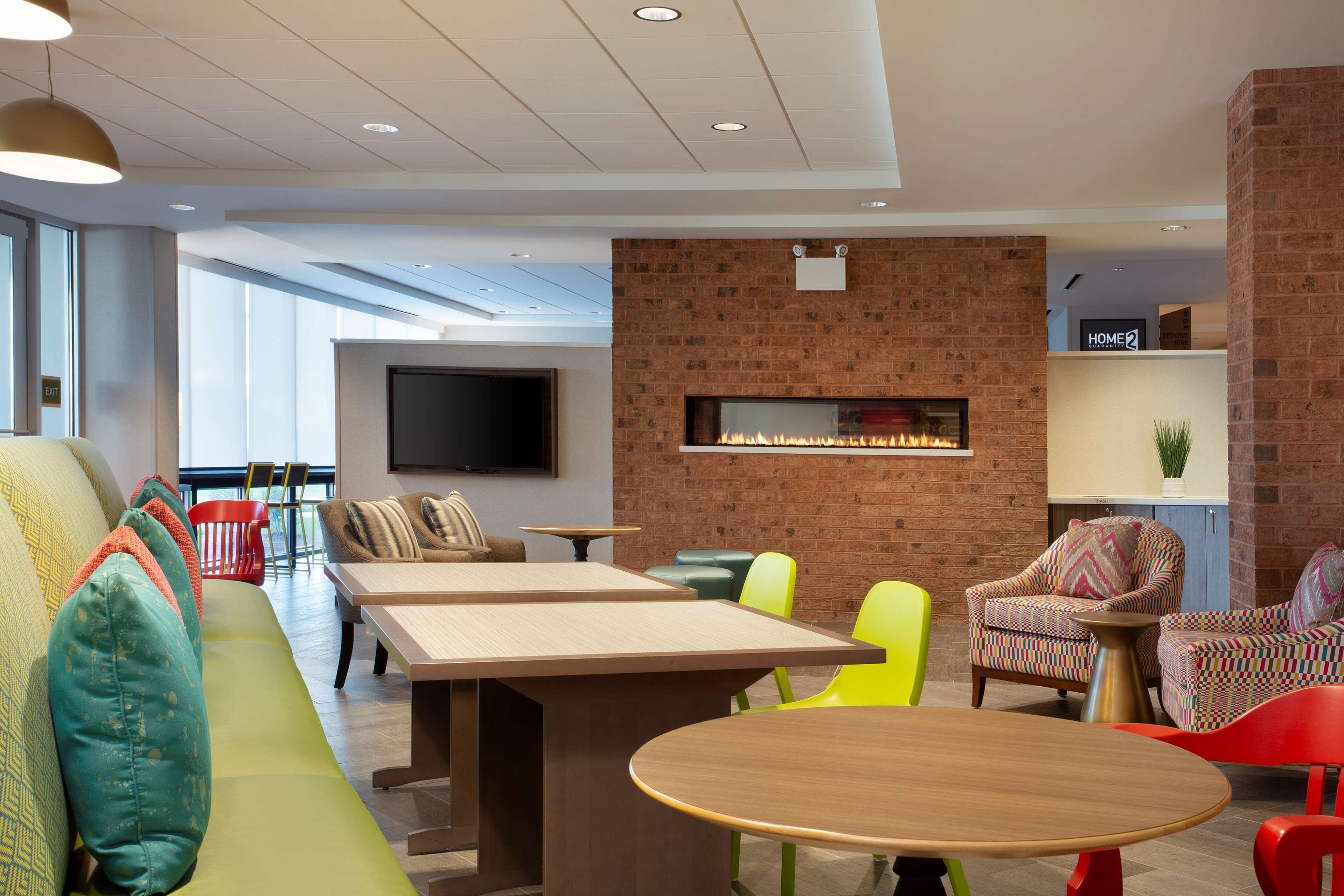 A modern lounge area with a brick wall, a fireplace, and a flat-screen TV. There are multiple seating options including a sofa, chairs, and a table.