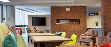 A modern lounge area with a brick wall, a fireplace, and a flat-screen TV. There are multiple seating options including a sofa, chairs, and a table.