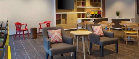 A modern hotel lobby with seating areas, a flat-screen TV, and a bar with shelves of bottles.