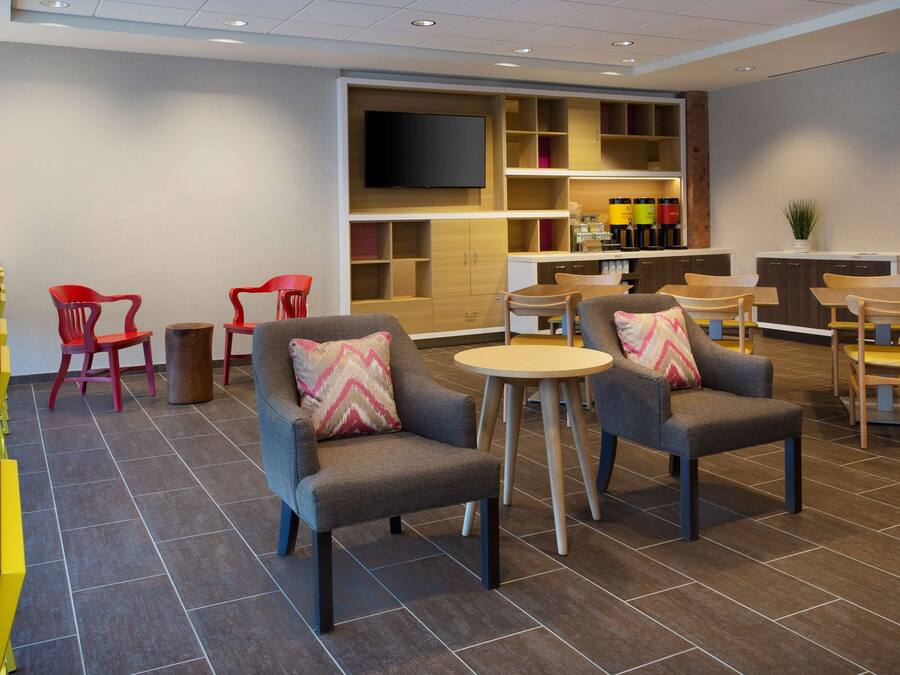 A modern hotel lobby with seating areas, a flat-screen TV, and a bar with shelves of bottles.