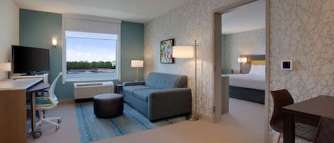 A hotel room with a desk, a sofa, a bed, and a dining area.