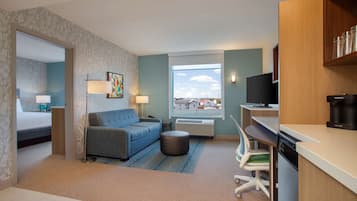 A compact hotel room with a bed, a sofa, a dining area, and a view of the cityscape.