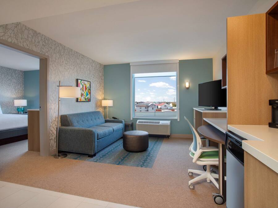A compact hotel room with a bed, a sofa, a dining area, and a view of the cityscape.