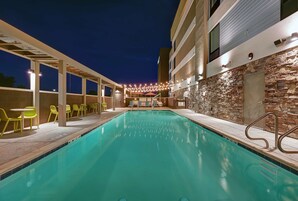 Una piscina con un muro de piedra y una zona techada con sillas amarillas.