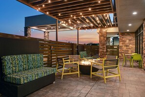 An outdoor seating area with wicker furniture, a fire pit, and string lights. - Home2 Suites by Hilton Tracy (Tracy)
