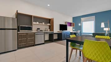 A modern kitchen with a built-in microwave, refrigerator, and wooden cabinets. There is a dining area with a table and chairs, and a television mounted on the wall.