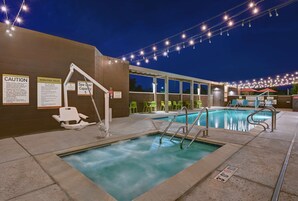 Zona de piscina con un cartel de aforo para usuarios de spa, señales de precaución y una silla accesible para personas en silla de ruedas.
