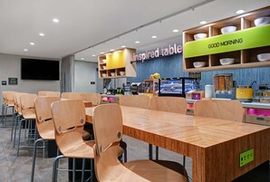 Un moderno comedor con mesas y sillas de madera, un cartel con la frase 'Good Morning' y otro cartel con la frase 'Inspired Table'.