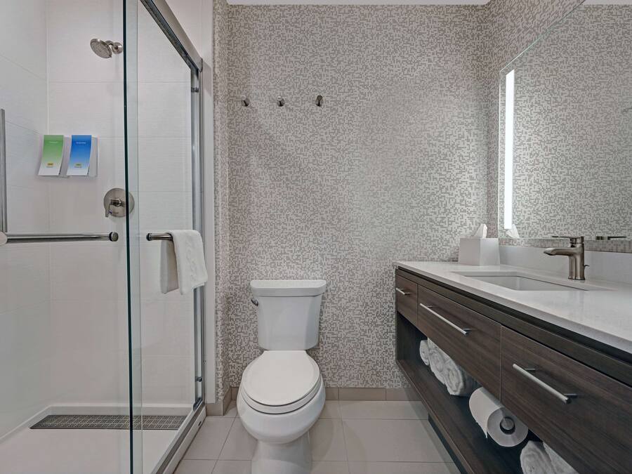 Un bany modern amb plat de dutxa de vidre, vàter blanc i un lavabo amb mirall i barra de tovalloles.