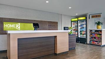 A hotel reception area with a reception desk, a digital kiosk, and two beverage dispensers labeled "freshly cold" and "cold".