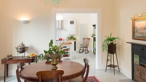 A dining area with a round table, chairs, a chandelier, a wall-mounted light, and a view into the kitchen. - Killadangan House (Westport)