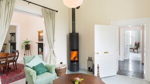 A cozy living room with a wood-burning stove, a comfortable armchair, a dining table, and a large window. - Killadangan House (Westport)