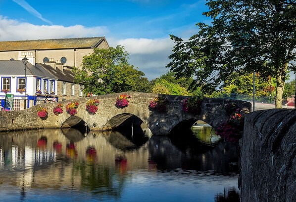 A stone bridge with flower boxes over a calm river, reflecting the surrounding buildings and trees.