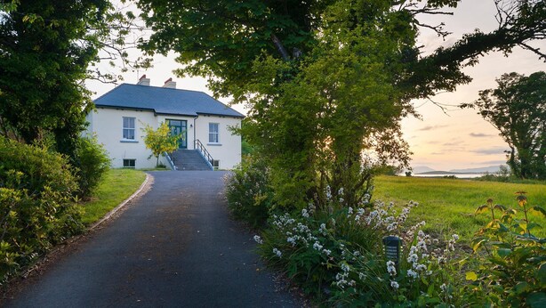 A house with a paved driveway leading to a front door, surrounded by lush greenery and flowering plants. - Killadangan House (Westport)