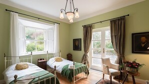 A bedroom with two beds, a chair, a table with flowers, and a chandelier. - Killadangan House (Westport)
