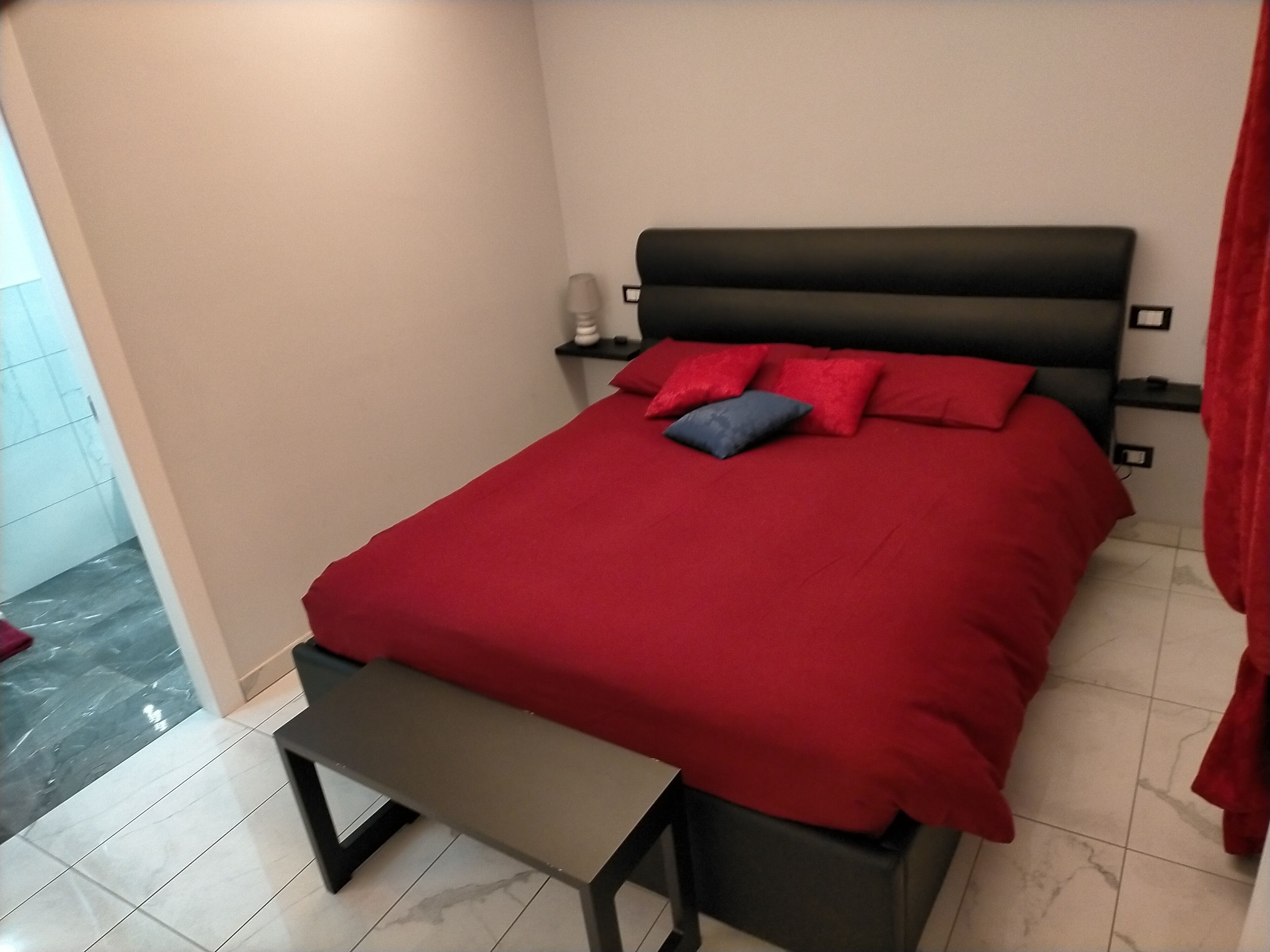 Un dormitorio con cama, almohadas, mesita de noche y una banca.