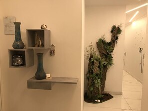 En hall med en hylla där vaser står uppradade och en väggmonterad växtkomposition.