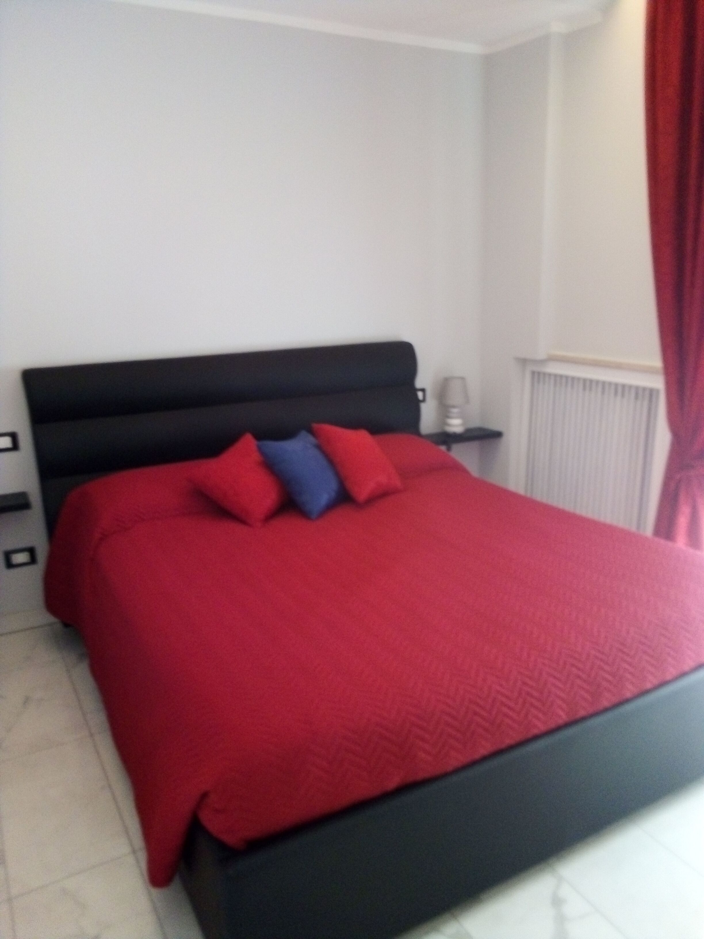 A bedroom with a black headboard, a red bedspread, and a red curtain.