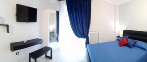 A bedroom with a bed, a bench, a TV mounted on the wall, and a window with curtains. - Casa della Zia Elsa (Verona)