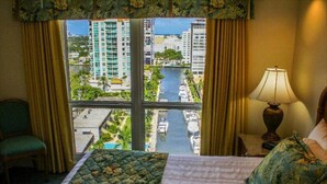 Una habitación de hotel con cama, una silla, una lámpara y vistas a un canal y edificios.