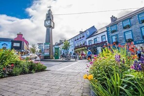 A town square with a clock tower, flower beds, and buildings with signage. - The Blue House (Westport)