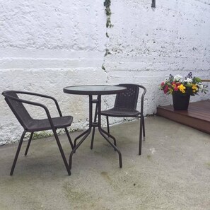 An outdoor seating area with two chairs and a table, a white textured wall, and a potted plant with flowers. - The Blue House (Westport)