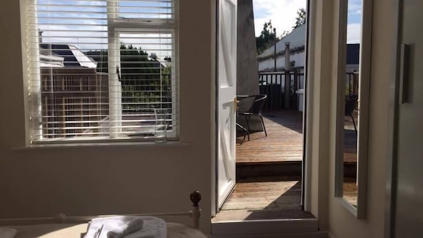A bedroom with a large window and an open door leading to a balcony with outdoor furniture. - The Blue House (Westport)