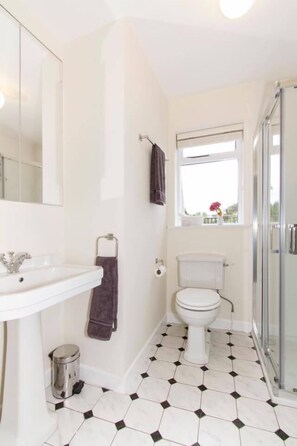 A bathroom with a white sink, toilet, and shower. There is a window above the toilet and a mirror above the sink. - The Blue House (Westport)