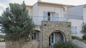 A two-story building with a stone facade, a balcony, and a small garden area with a tree.