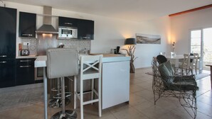 A modern kitchen with dark cabinets, a central island, and bar stools. There is a dining area with a table and chairs.