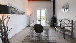 A dining area with a white table, chairs, and a black lamp. There is a fireplace and a bench in the background.