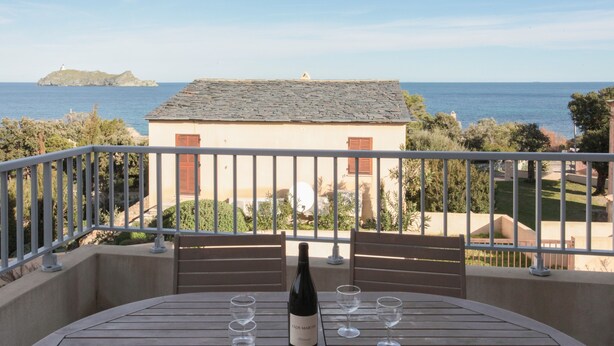 A balcony with a table, a bottle of wine, and four glasses.
