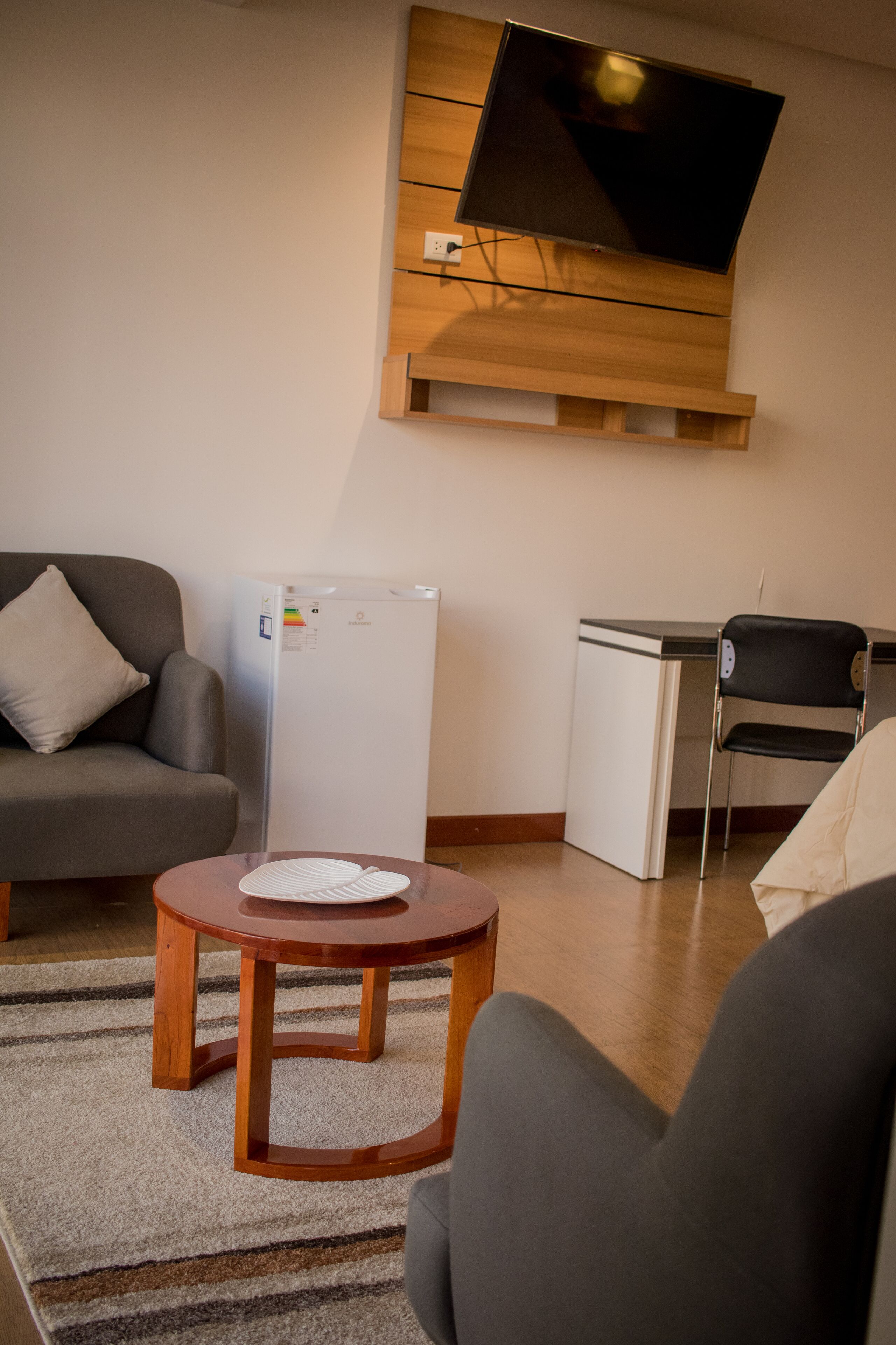 Un espacio habitable compacto con un sofá, una mesita redonda, un refrigerador, un escritorio y una silla.