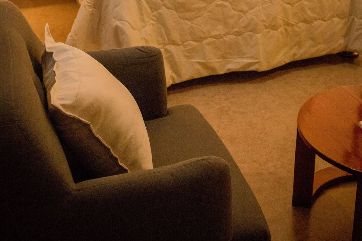 Ein Hotelzimmer mit einem großen Bett, zwei Nachttischlampen, einem grünen Sessel und einem kleinen Holztisch.