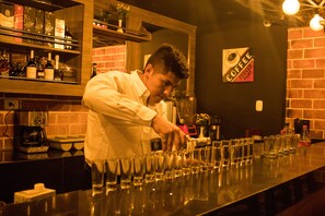 A bar area with a bartender preparing drinks. There are shelves with bottles and a sign indicating the bar serves coffee. - Murano Hotel (Moyobamba)