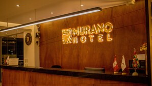 A reception desk with a wooden panel wall and illuminated hotel name. - Murano Hotel (Moyobamba)