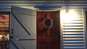 A house with a red door, a wreath hanging on it, and a snow-covered front step. - Cozy cottage tucked away in the woods (Townshend)